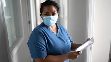 A health care worker wearing blue scrubs and a face mask