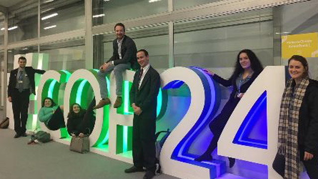 Students pose next to a green and blue illuminated sign that says COP24