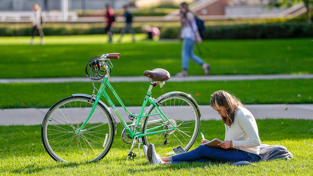 A student studies on a grassy area next to a bicycle