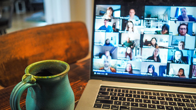 A mug of coffee sits next to a laptop with people on a Zoom call