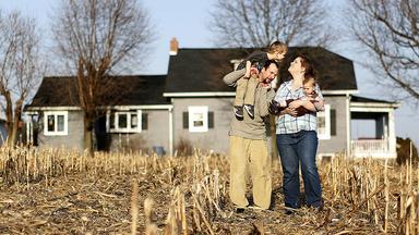 Man, woman and two children outside a house near a cornfield