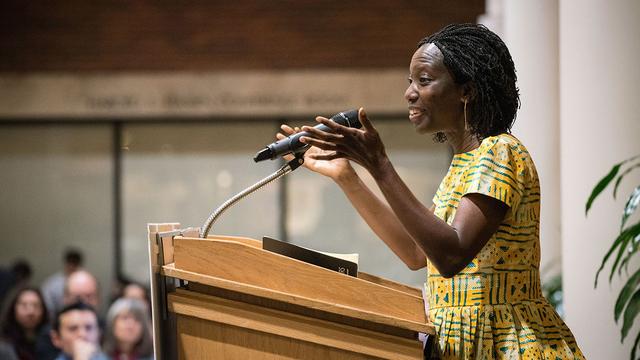 Agnes Igoye stands behind a podium speaking to an audience in the Humphrey School atrium. 
