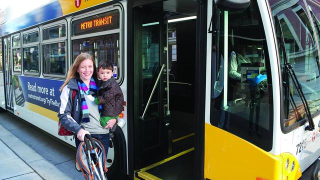 Woman holds a small child on the sidewalk outside a Metro Transit bus