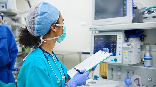 A nurse wearing medical garb looks at a computer monitor