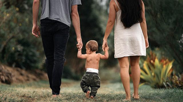 A man and woman hold hands with a toddler