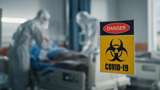 Hospital ward for coronavirus patients, with health care providers in gowns and masks, and a covid-19 biohazard sign on the window