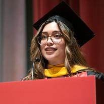 Ruby DeBellis stands behind a podium speaking at the 2023 Humphrey School commencement ceremony