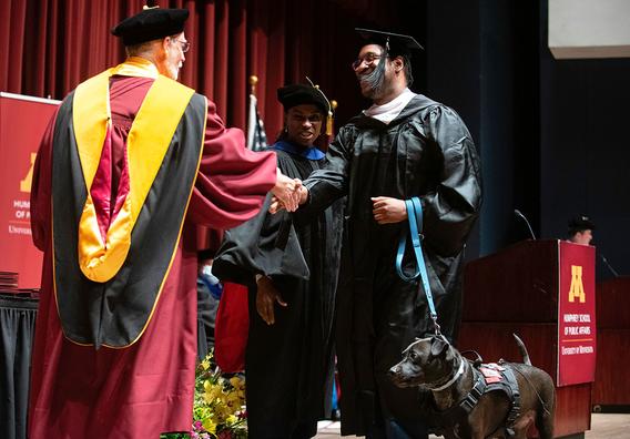 MPA graduate Corey Dawson and his dog Oscar walk across the stage at 2022 commencement ceremony