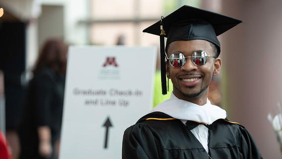 Photo of Ruthvin Gardiner in commencement regalia and sunglasses in May 2023.