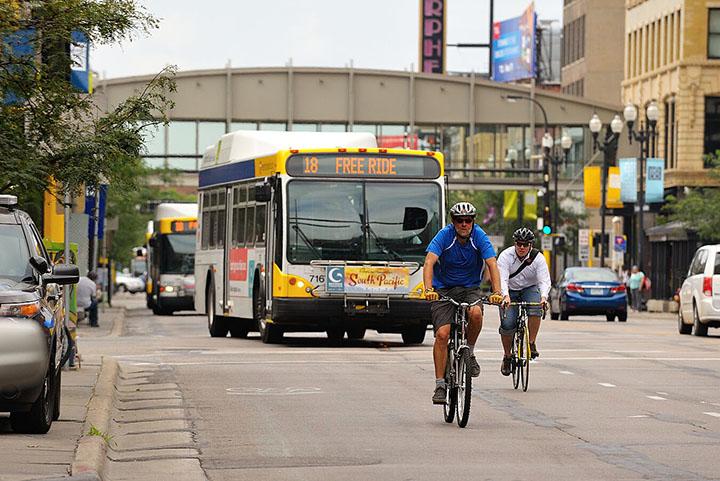 Traffic on a city street, including two bicyclists, a bus, and several cars