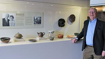 Walter Mondale stands next to a display of Joan Mondale's pottery at the Humphrey School