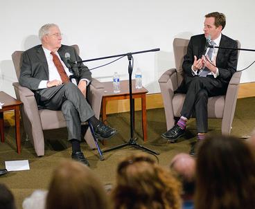 Walter Mondale and Charlie Savage sit on stage in the Humphrey School auditorium.