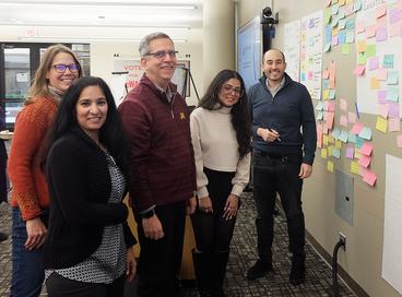 Group photo of several people standing in front of a wall on which sticky notes are attached
